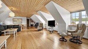 A spacious loft with a high ceiling, wooden beams, a dining area, a sofa, a TV, and a window with a view.