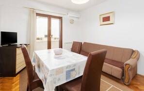 A room with a dining table, chairs, a sofa, a TV, and a window with curtains.