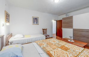A bedroom with two beds, a wooden chair, a wardrobe, and a bedside table.