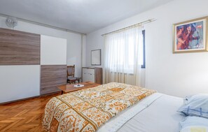 A bedroom with a bed, a wooden dresser, a chair, a desk, and a painting on the wall.