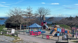 A playground with slides and climbing structures, surrounded by trees and a view of the sea. - Stone and vacation apartment with covered parking space and pool access. (Saint-Raphaël)