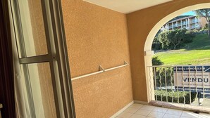 A room with a large window, a tiled floor, and a view of a building with a sign. - Stone and vacation apartment with covered parking space and pool access. (Saint-Raphaël)