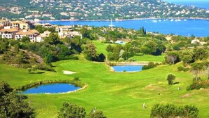 A golf course with bunkers, a pond, and a view of a coastal town with houses and a mountain in the background. - Stone and vacation apartment with covered parking space and pool access. (Saint-Raphaël)