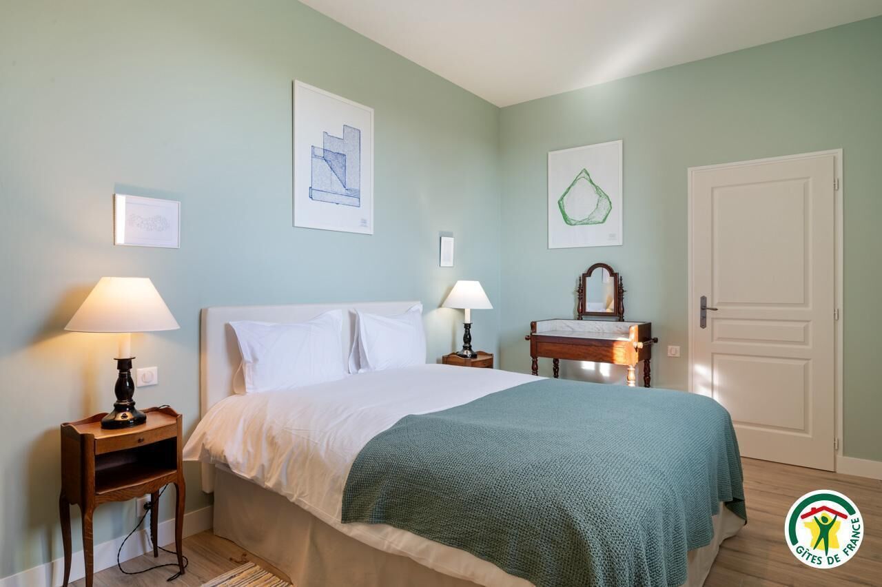 A bedroom with a bed, two bedside tables with lamps, a mirror, and framed artwork on the walls.