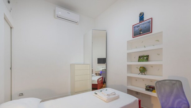 A bedroom with a bed, a dresser, a mirror, a chair, and a shelf with books and a globe. - GIACOSA, 71 – Spacious apartment for 6 (Milano)