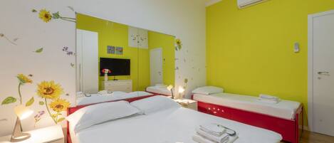A hotel room with a bed, a bedside table, a mirror, a red bedside table, a white door, and an air conditioning unit.