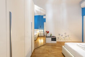 A modern hotel room with a mirrored wardrobe, a bed, a small bedside table with a vase of flowers, and a wall decal. - GIACOSA, 71 – Spacious apartment for 6 (Milano)