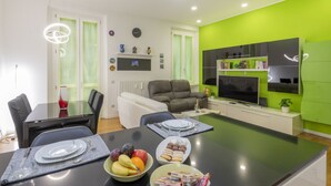 A modern living room with a dining area, green walls, a flat-screen TV, and a sofa. - GIACOSA, 71 – Spacious apartment for 6 (Milano)
