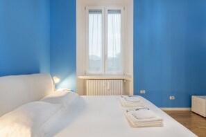 Une chambre à coucher avec un lit, une fenêtre avec des rideaux, un radiateur et une table de chevet avec une lampe.