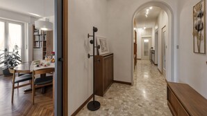 A hallway with a tiled floor, a coat rack with a picture, and a wooden table with chairs. - Otto Novembre, 3 – Spacious and Elegant with a View (Milano)