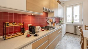 A modern kitchen with red tiles, wooden cabinets, a gas stove, and a window with a view. - Otto Novembre, 3 – Spacious and Elegant with a View (Milano)