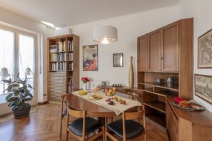A dining area with a wooden table, chairs, a bookshelf, and a decorative vase. - Otto Novembre, 3 – Spacious and Elegant with a View (Milano)