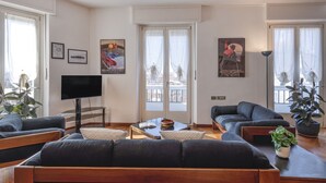 A modern living room with a flat-screen TV, two sofas, a coffee table, and a balcony view. - Otto Novembre, 3 – Spacious and Elegant with a View (Milano)