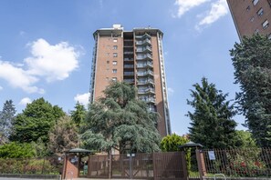 Een hoog appartementencomplex van baksteen met meerdere balkons, omringd door bomen en een hekwerk.
