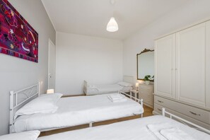 A room with two beds, a wardrobe, a mirror, and a wall-mounted artwork.
