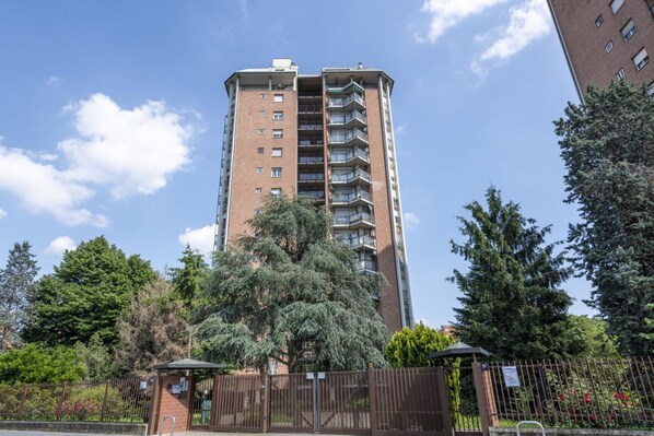 Ein hohes Backsteinwohnhaus mit mehreren Balkonen, umgeben von Bäumen und einem abschließbaren Eingang.