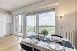 A dining area with a table set for two, a bowl of fruit, and a vase of flowers.