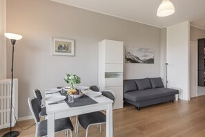 A modern living room with a grey sofa, a dining table with chairs, a radiator, and artwork on the walls. - Omodeo, 19 – Spacious and Panoramic (Milano)