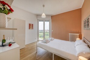 A bedroom with a bed, bedside table, a radiator, a window, and a balcony.