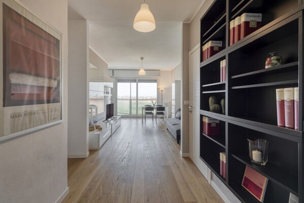 A modern interior with a hallway leading to a dining area, a bookshelf with books, and a large framed picture on the wall.