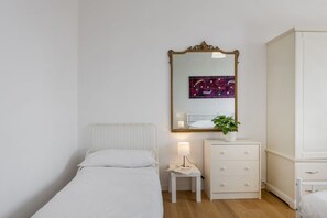 A bedroom with a bed, a bedside table with a lamp, a dresser, and a mirror.