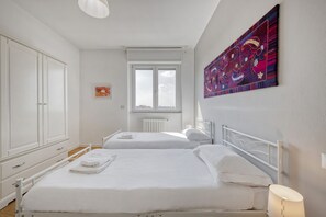 A bedroom with two beds, a radiator, a window, and a painting on the wall. - Omodeo, 19 – Spacious and Panoramic (Milano)