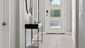 A hallway with a door leading to a room, a black console table with a mirror, and a light fixture. - Family escape: pool, hot tub & resort access (Kissimmee)