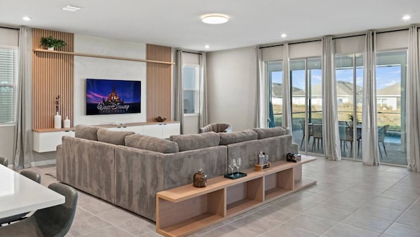 A modern living room with a large sectional sofa, a flat-screen TV, and a glass door leading to a balcony. - Family escape: pool, hot tub & resort access (Kissimmee)