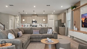 A modern living room with a grey sectional sofa, a round coffee table, and a TV mounted on the wall. - Family escape: pool, hot tub & resort access (Kissimmee)
