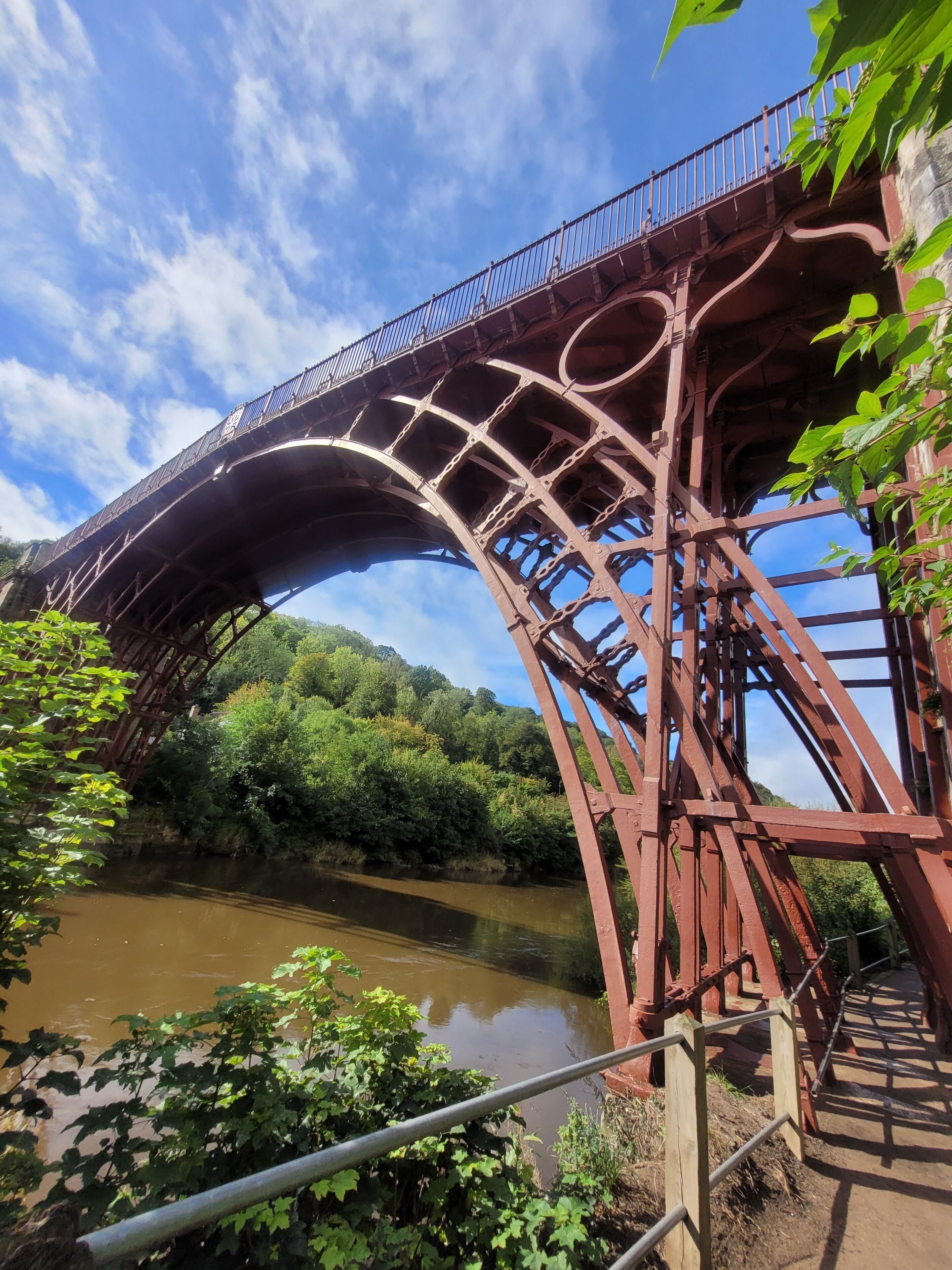 Un puente metálico grande y arqueado sobre un río, rodeado de follaje y árboles.