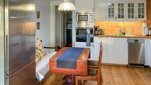 Una cucina funzionale con frigorifero, microonde, forno e lavastoviglie. C'è un tavolo da pranzo con sedie e una lampada a sospensione.