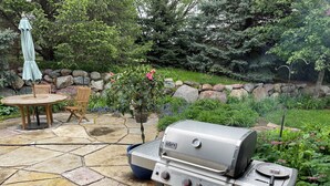 Une terrasse avec une table en pierre, des chaises en bois et un barbecue portable.