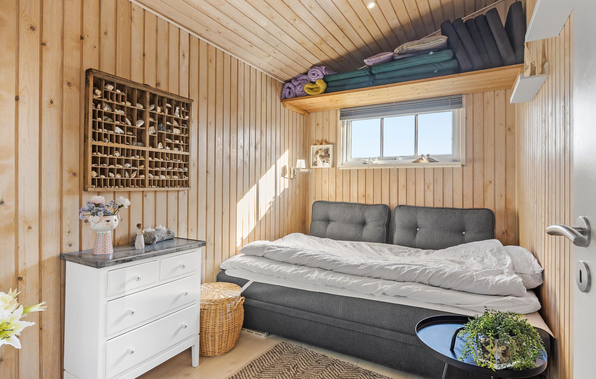 Un dormitorio con cama, cómoda, ventana y estante con mantas dobladas.