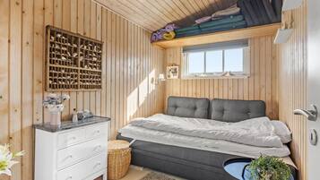 Un dormitorio con cama, cómoda, ventana y estante con mantas dobladas.