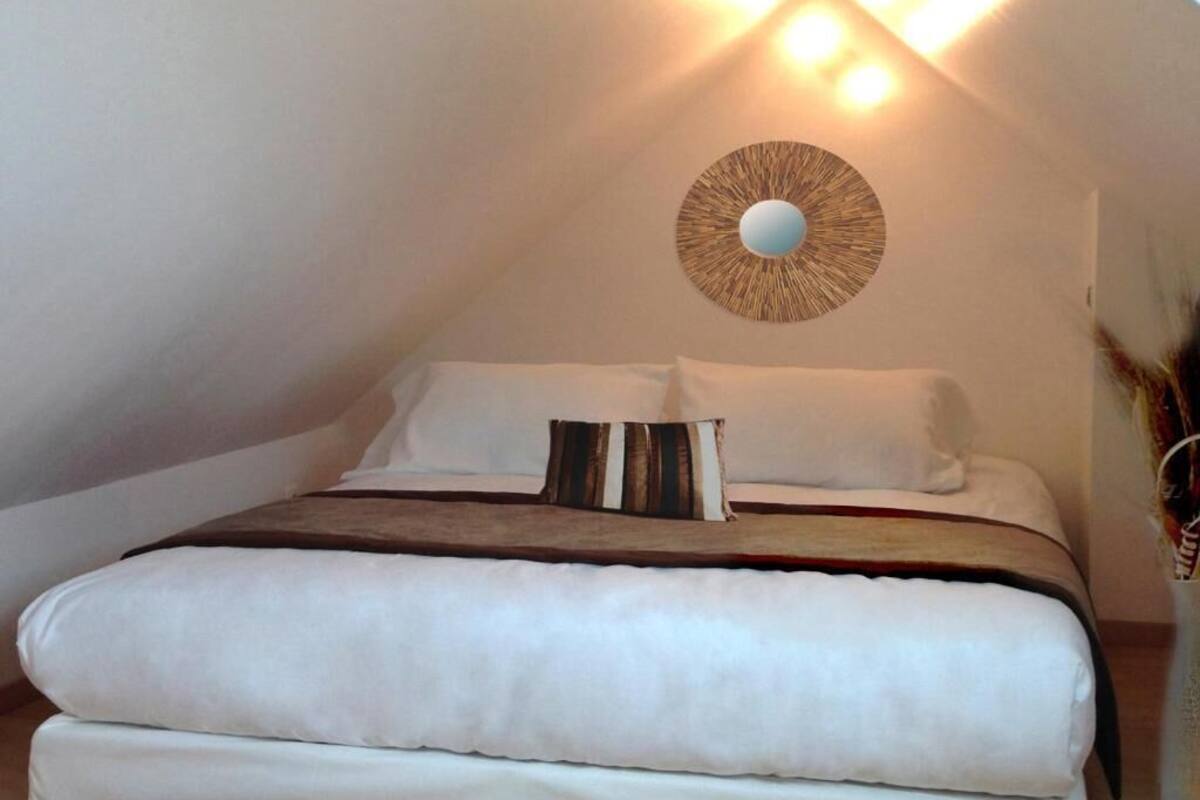 Quarto com cama, almofadas, luminária na parede e um espelho decorativo.