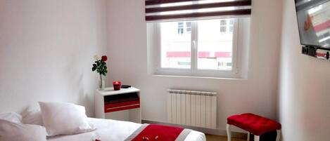 A bedroom with a bed, bedside table, window, radiator, and a red bench.