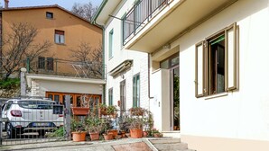 Un immeuble résidentiel à la façade blanche, doté d’un balcon avec une rambarde en métal, et une voiture garée devant.
