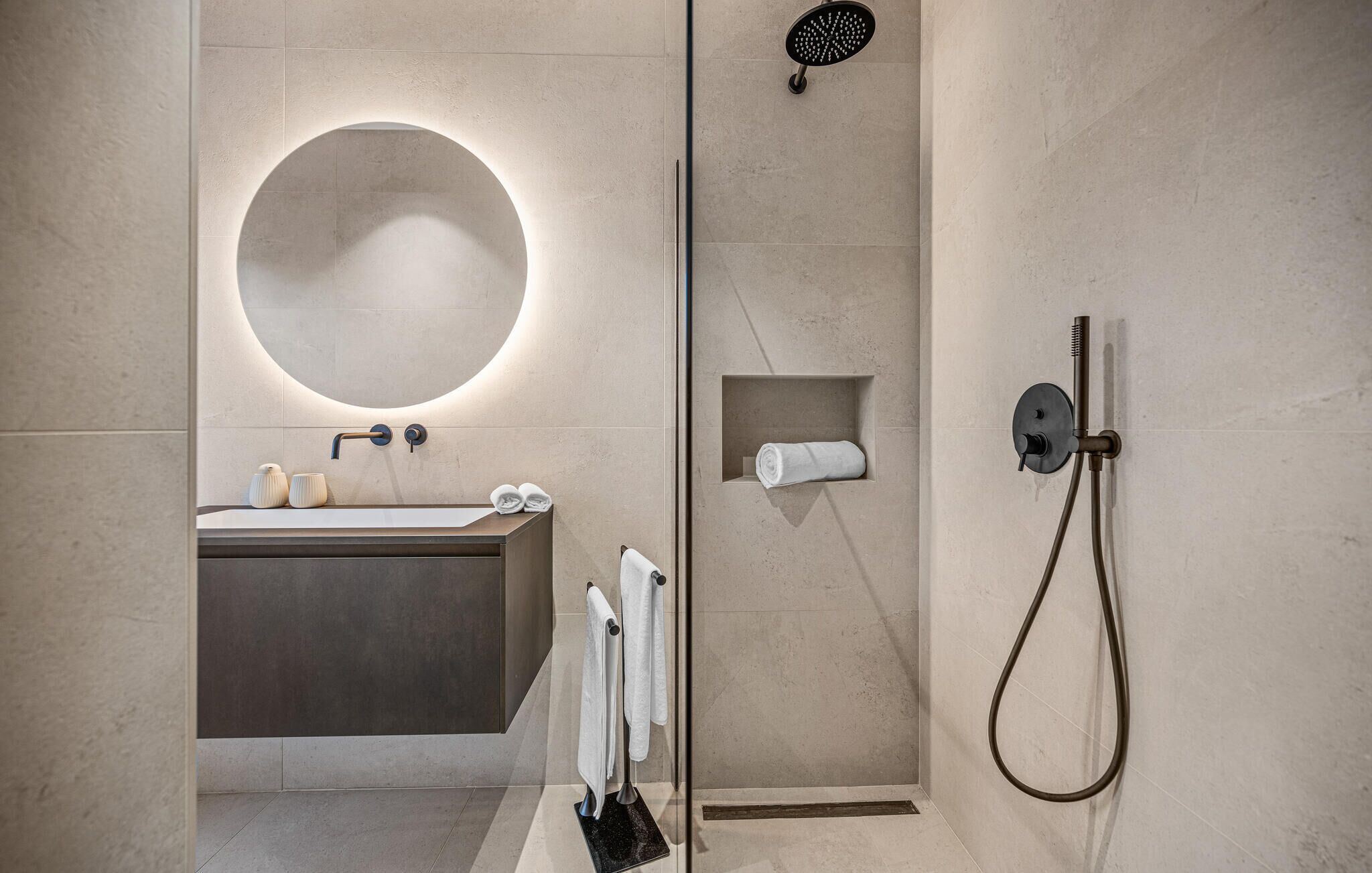 A modern bathroom with a round mirror, a sink, a shower, and a towel rack.