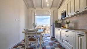 Une cuisine avec des meubles blancs, une table à manger avec des chaises et un sol à carreaux.