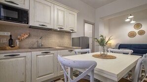 A modern kitchen with white cabinetry, a microwave, and a refrigerator. There is a dining table with chairs and a vase with flowers.