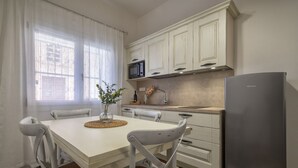 A kitchen with white cabinets, a stainless steel refrigerator, a microwave, and a dining table with chairs.