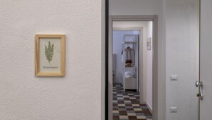 A hallway with a framed botanical illustration on the wall, a checkered floor, and a door leading to a room with a white wardrobe.