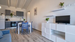 Eine moderne Küche mit weißen Schränken, ein Essbereich mit blauen Stühlen und ein Fernseher auf einem weißen Schrank.