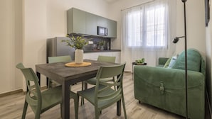 Un espacio habitable compacto con una mesa de comedor, sillas, un sofá, una kitchenette y un ventanal con cortinas.