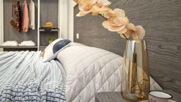 Una cama bien hecha con una colcha acolchada, un florero con flores y una taza de café sobre una mesita de noche.