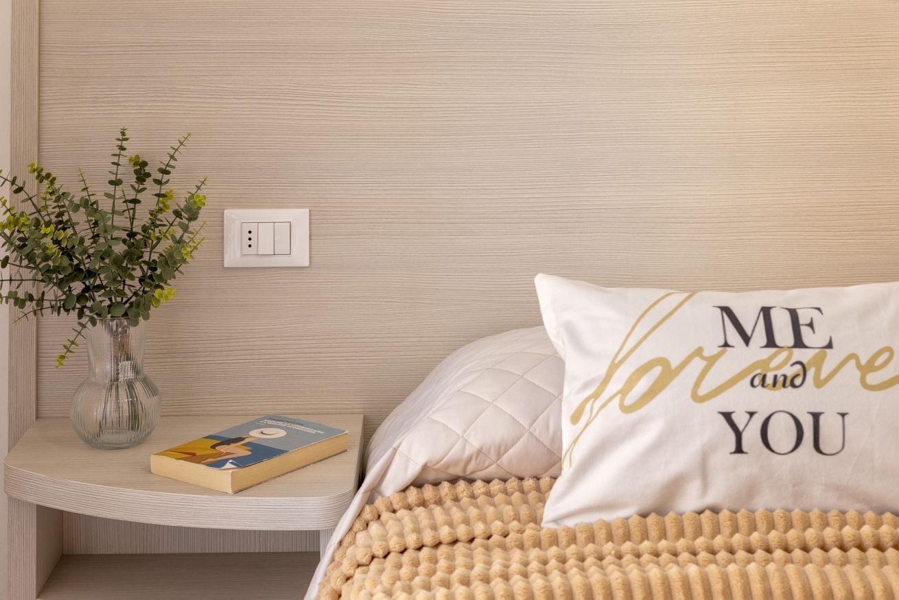 A neatly arranged bedroom with a bed, a bedside table, a book, and a vase with flowers.