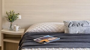 A neatly made bed with a magazine, a pillow with "love" embroidered on it, a small table with a vase and a mug, and a wall with a light wood finish. - Casa Erica. Apartment a few steps from the historic center. (Olbia)