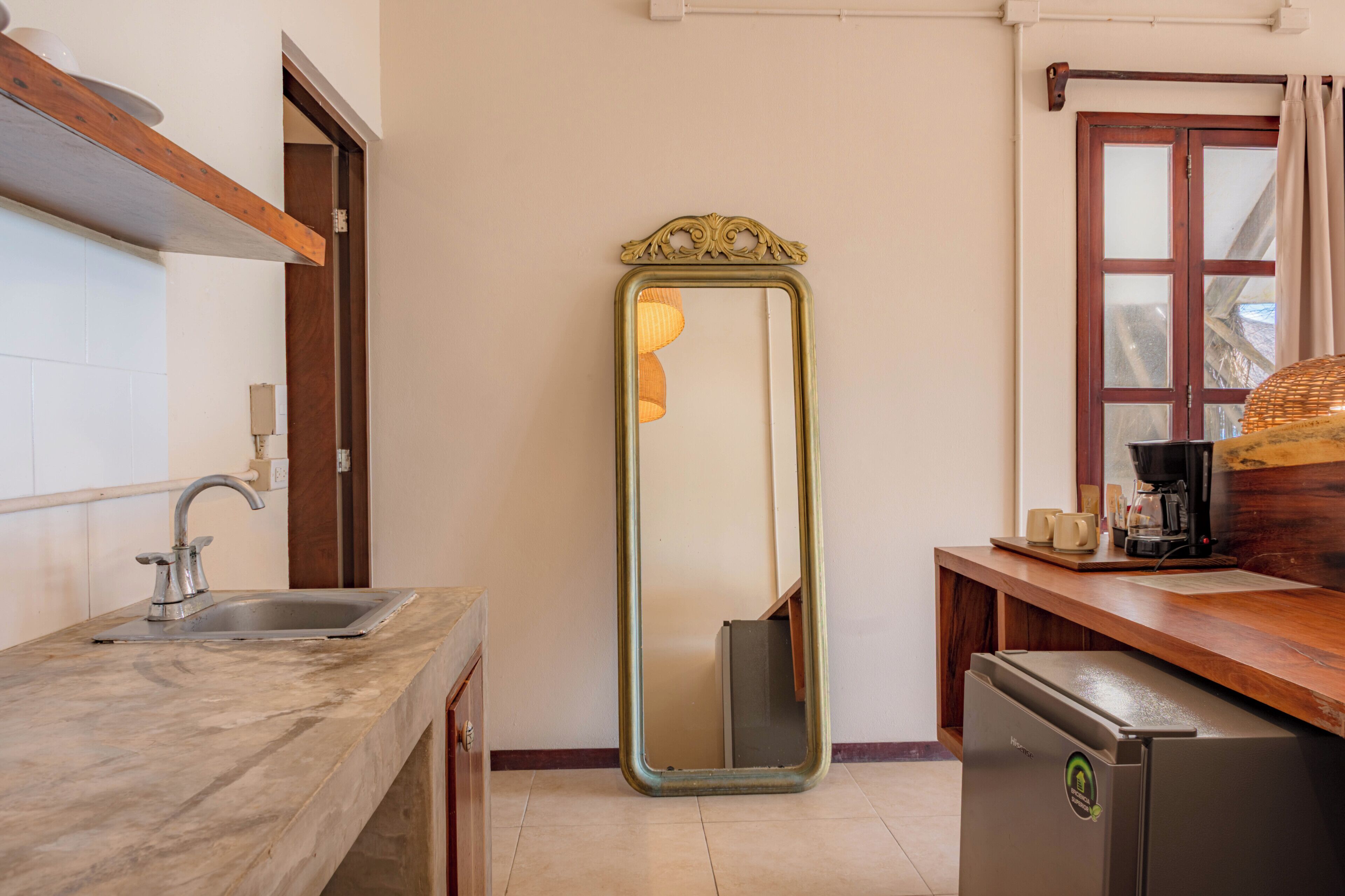 A kitchen with a sink, a mirror, a refrigerator, and a window with curtains.