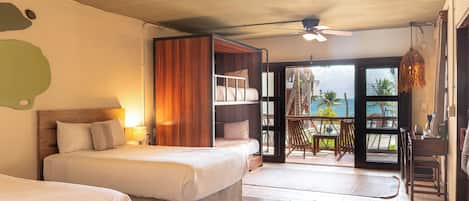 A hotel room with a bed, a ceiling fan, a balcony with a view of the ocean, and a dining area with chairs.