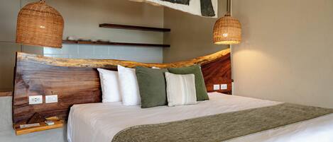A bed with a wooden headboard, white bedding, and a green throw blanket. There are two wicker pendant lights above the bed.